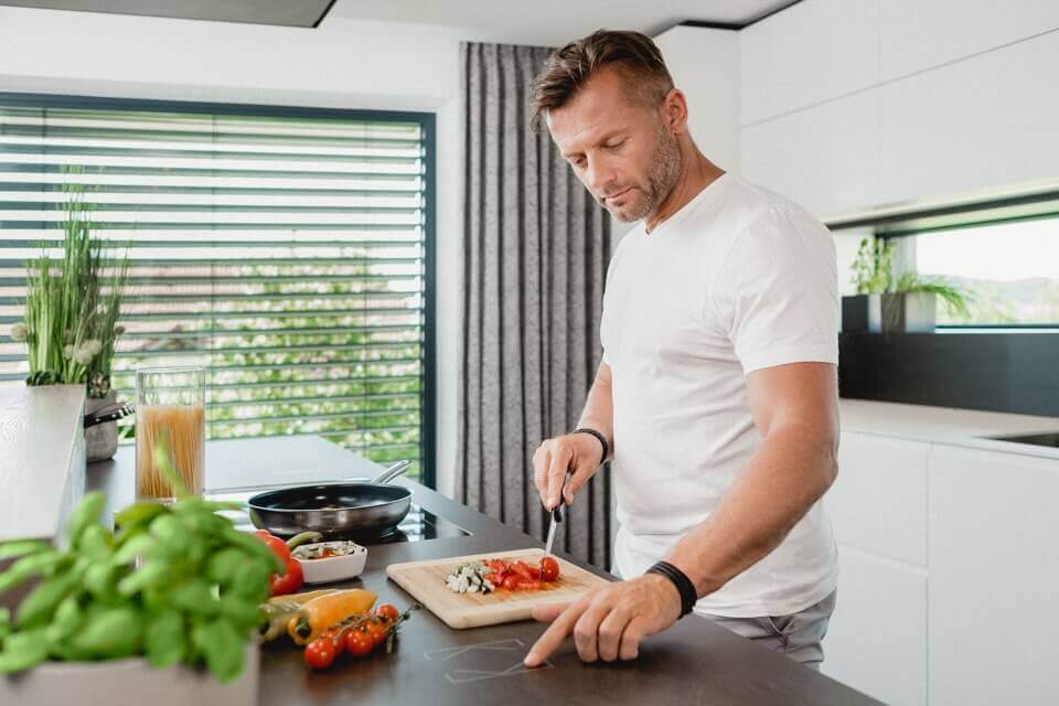 muž krájí zeleninu a ovládá při tom chytré tlačítko integrované v kuchyňské desce